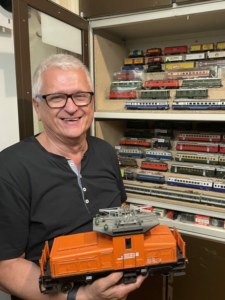 Foto: Inhaber mit einer orangen Modell-Diesellok vor Regalen voller Modelleisenbahnen